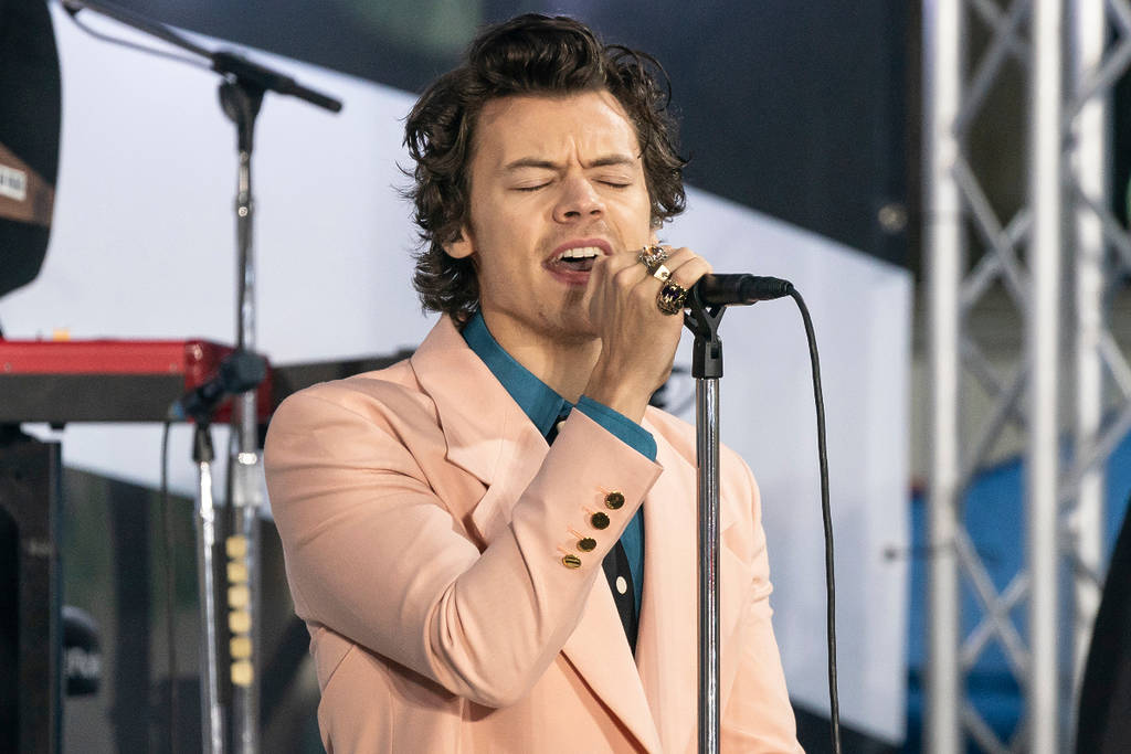 Image shows Harry Styles singing into a microphone while wearing a suit on stage.