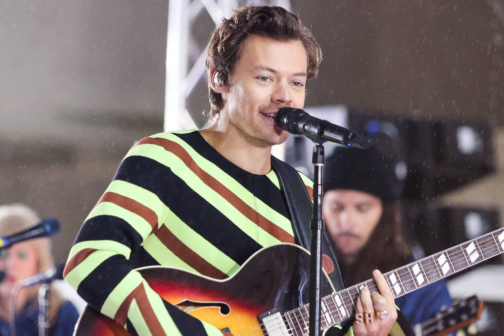 Image shows Harry Styles playing guitar while performing on stage.