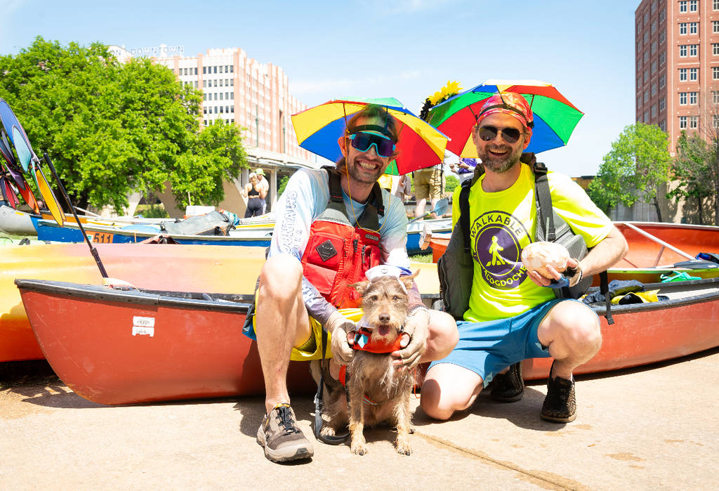 La imagen muestra a dos participantes de la regata de la Asociación Buffalo Bayou en Houston posando con su barco y su perro.
