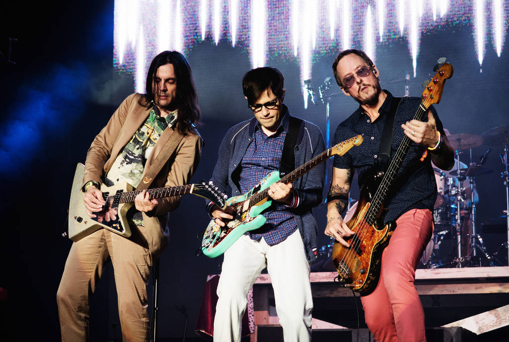 La imagen muestra a Weezer actuando en el escenario.