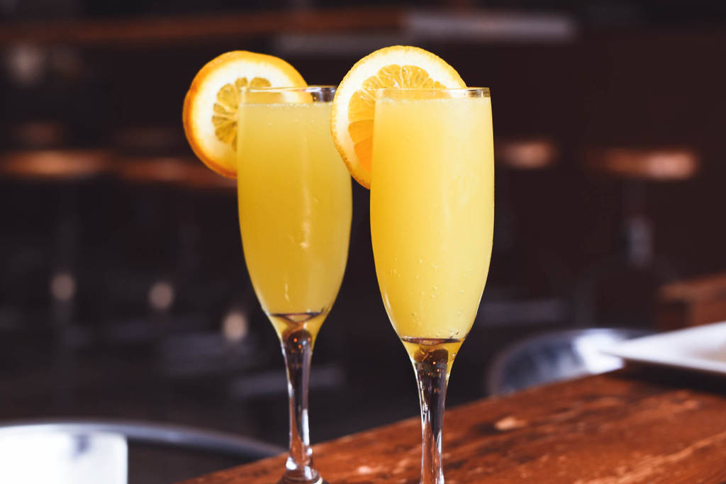 Image shows two mimosas displayed with orange slices placed on the rim of the glasses.