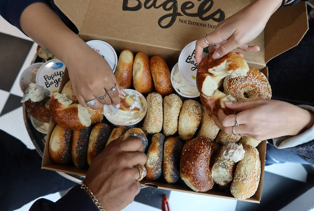 La imagen muestra a un grupo de personas cogiendo bagels de una caja de PopUp Bagels.