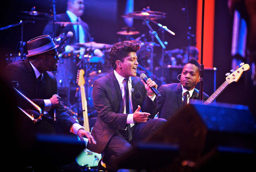 La imagen muestra a Bruno Mars cantando durante una actuación en el escenario.