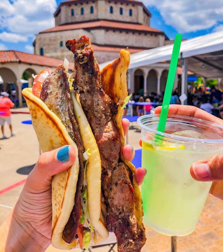 Image shows someone holding up a gyro and lemonade at Houston Greek Fest. 