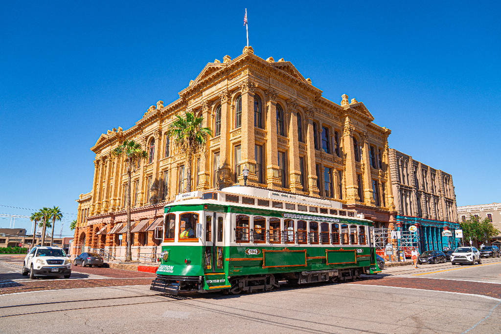 Image shows a vintage rail trolley with a building in the background at Historic Downtown in Galveston.