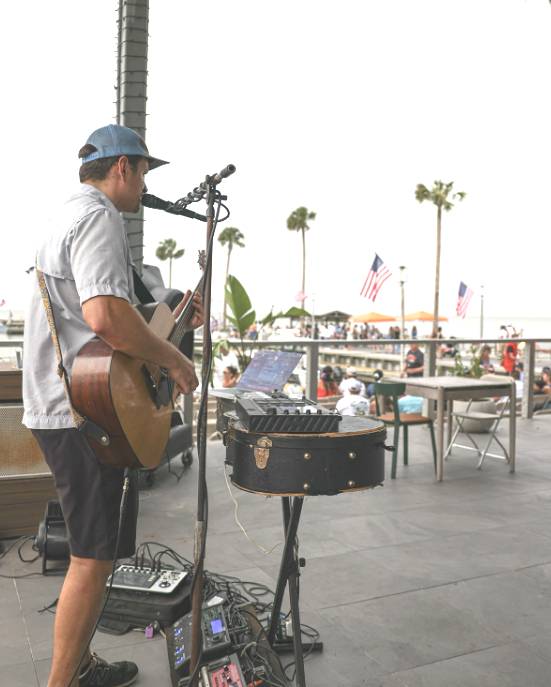 Image shows a musician playing guitar and singing at Pier 6 & Oyster House July Fourth celebration. 