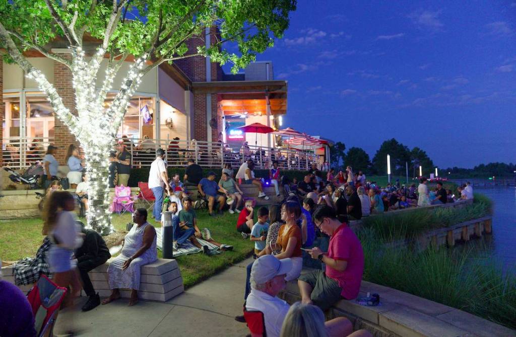 Image shows community event at Kings Harbor Waterfront Village at evening with people gathered around the waterfront. 