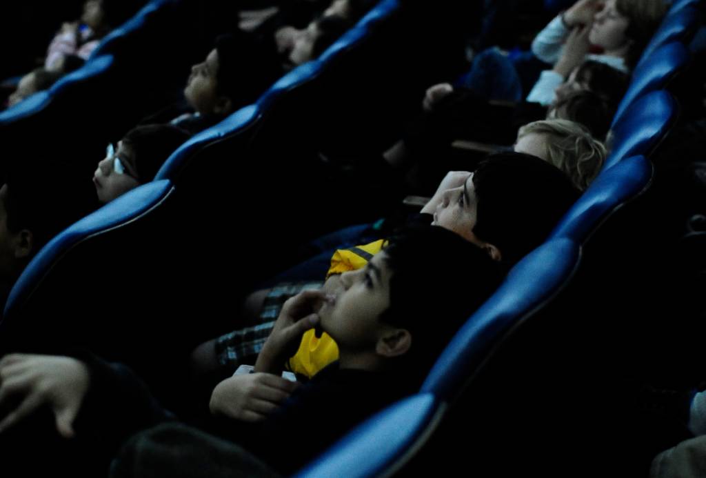 La imagen muestra a personas sentadas en sus butacas viendo la pantalla en el Planetario Burke Baker de Houston. 