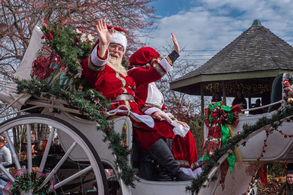 La imagen muestra a Papá Noel y a la señora Noel saludando a la multitud durante un desfile navideño.