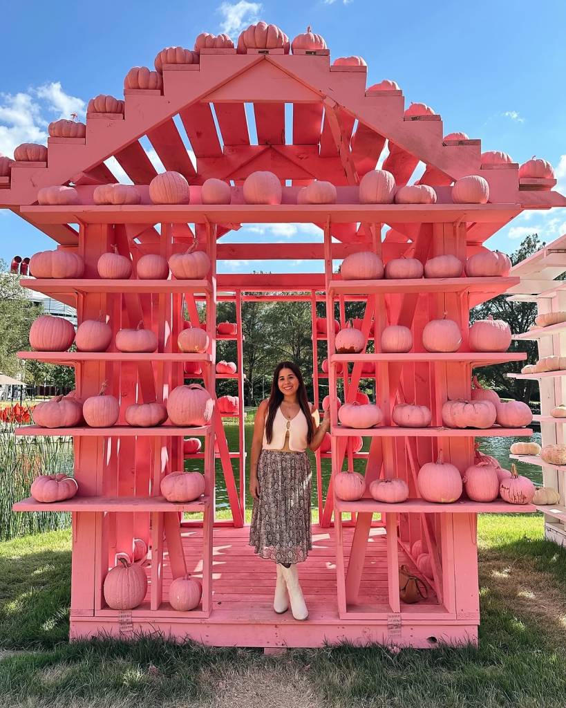 La imagen muestra a una mujer posando en una casa de colores vivos en el Festival de la Calabaza de Houston. 
