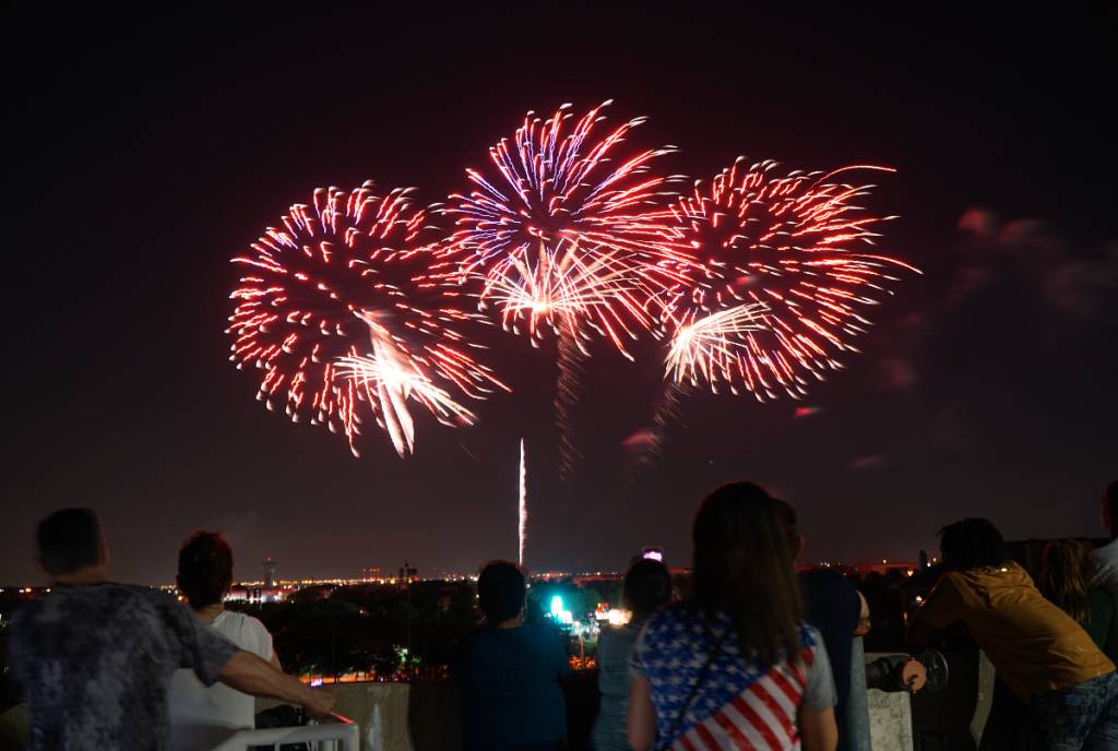 La imagen muestra a una multitud contemplando los fuegos artificiales que se disparan al fondo.