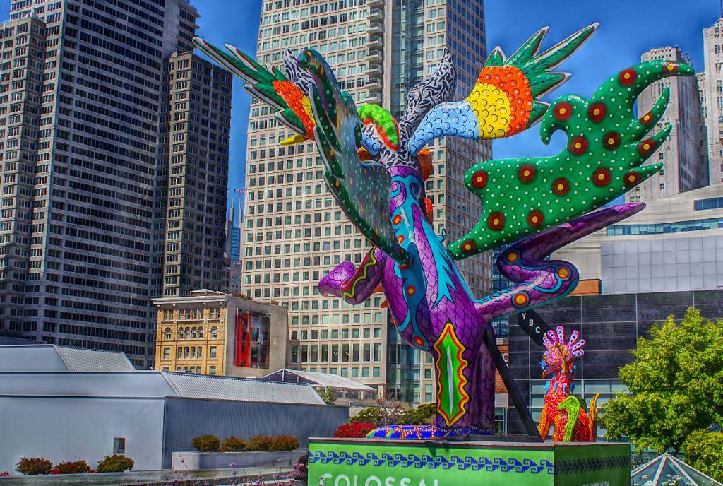 La imagen muestra una gran escultura de estilo mexicano con edificios de Houston al fondo.
