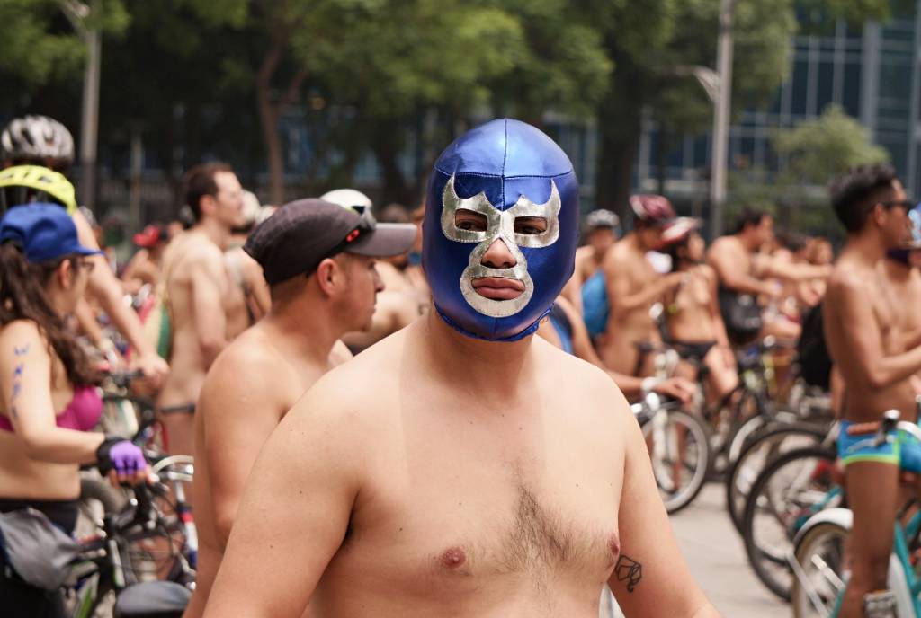 La imagen muestra una concentración de ciclistas desnudos en la que destaca un hombre que lleva una máscara de lucha libre mexicana.