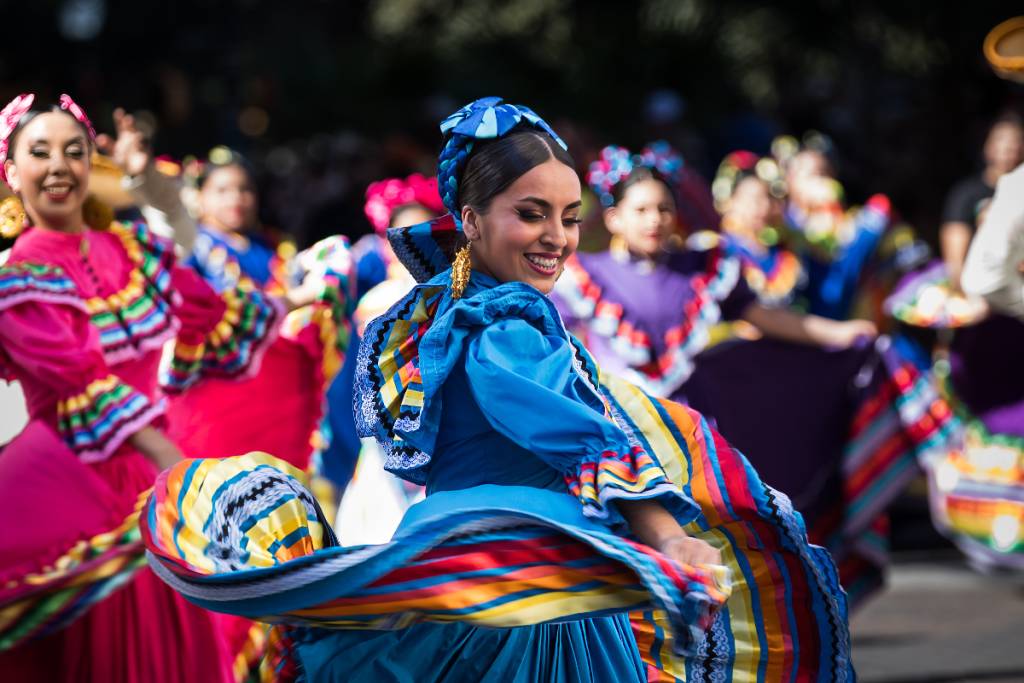 La imagen muestra a bailarines del Ballet Folclórico durante un desfile.