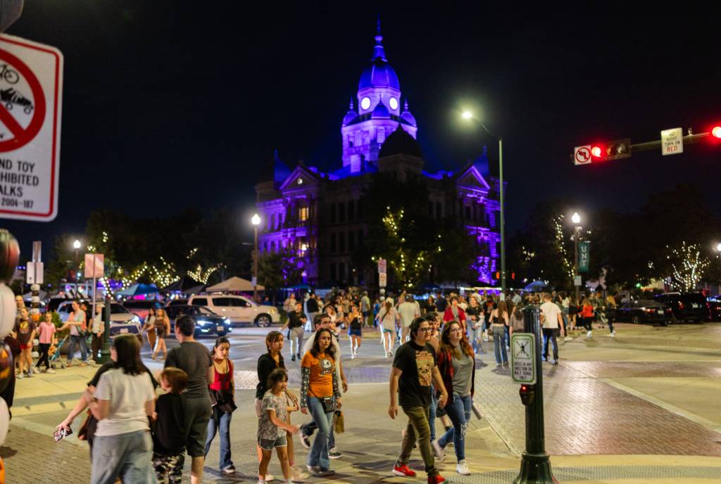 La imagen muestra a un grupo de personas paseando por Denton con el juzgado al fondo, iluminado con una luz siniestra.
