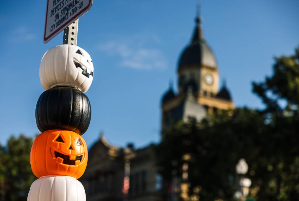 La imagen muestra un poste indicador en Denton adornado con mini calabazas de Halloween, con el juzgado al fondo.