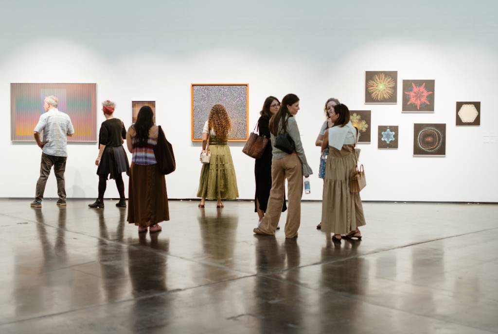La imagen muestra a un grupo de personas en una galería de arte durante la feria Untitled Art de Houston.