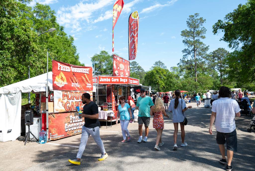 La imagen muestra a un grupo de personas disfrutando del Bayou City Art Festival.