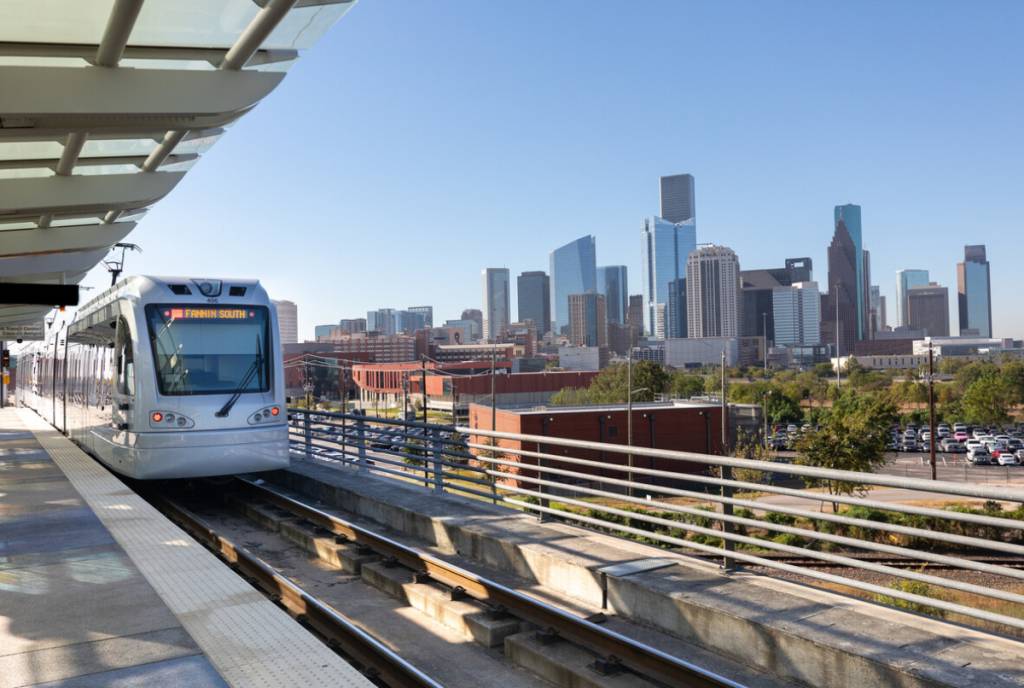 La imagen muestra el metro de Houston con el perfil de la ciudad al fondo.