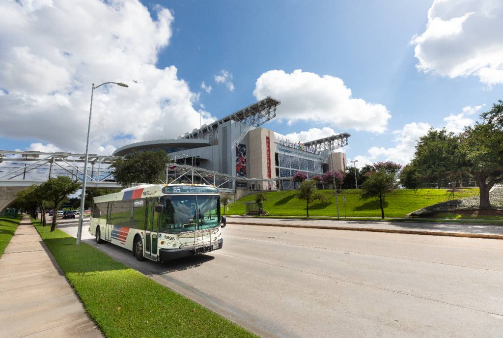 La imagen muestra un autobús de Houston en la calle con un edificio detrás.