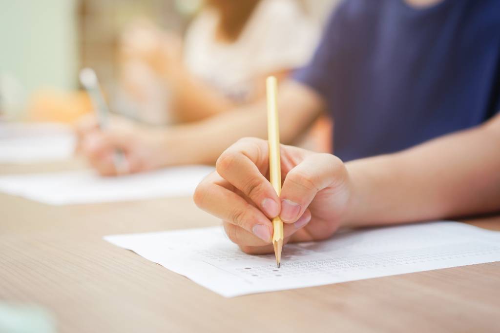 La imagen muestra a un alumno escribiendo con un lápiz.