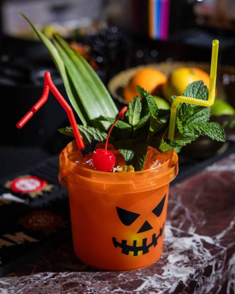 Image shows a themed cocktail in a cup decorated like a jack-o-lantern.