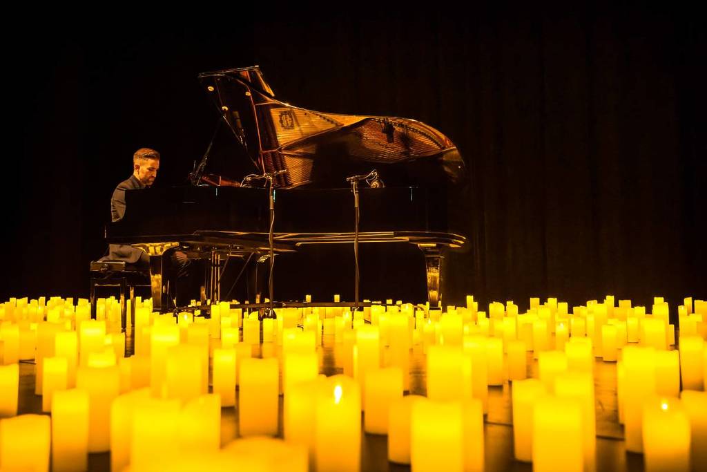 A musician playing the piano amid a sea of candles