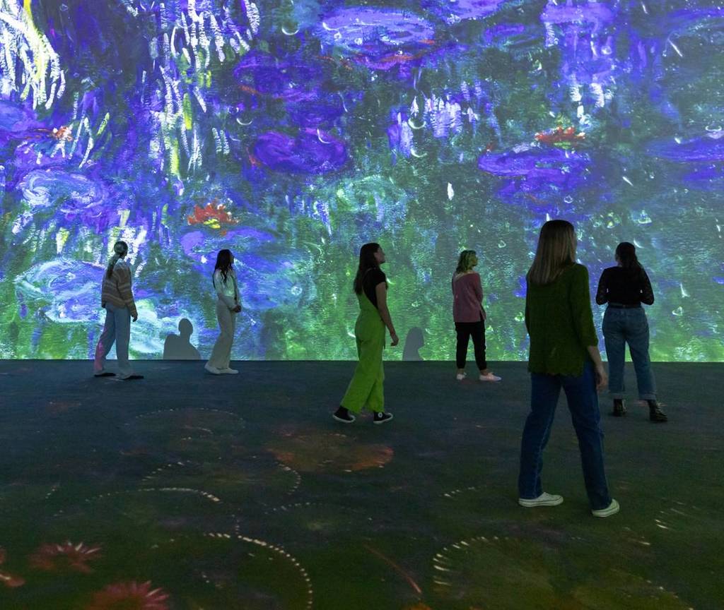 a group of people watch a 360-degree show of Monet's art at Monet: The Immersive Experience