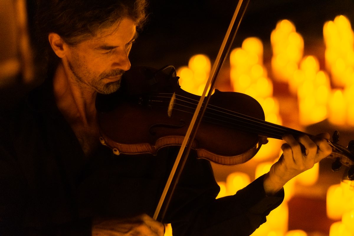Musiker spielt bei einem Candlelight-Konzert auf einer Violine, leuchtende Kerzen im Hintergrund
