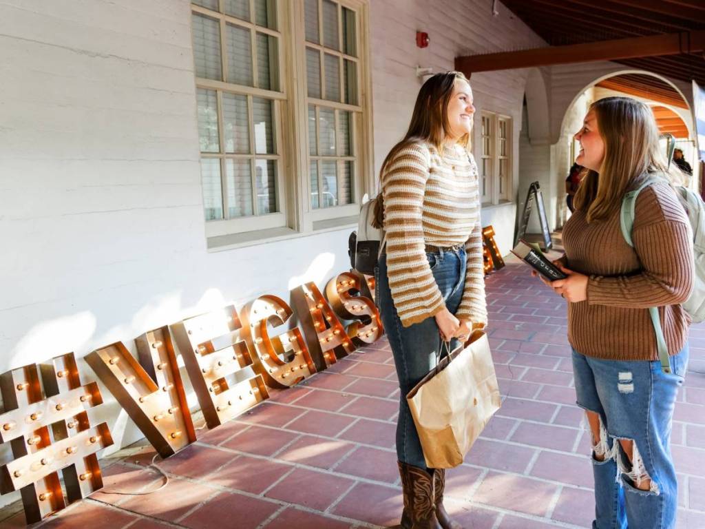 2 girls chatting in front of a Las Vegas Book Festival sign