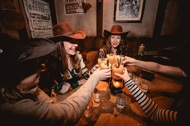people in cowboy hats cheersing their drinks at moonshine saloon