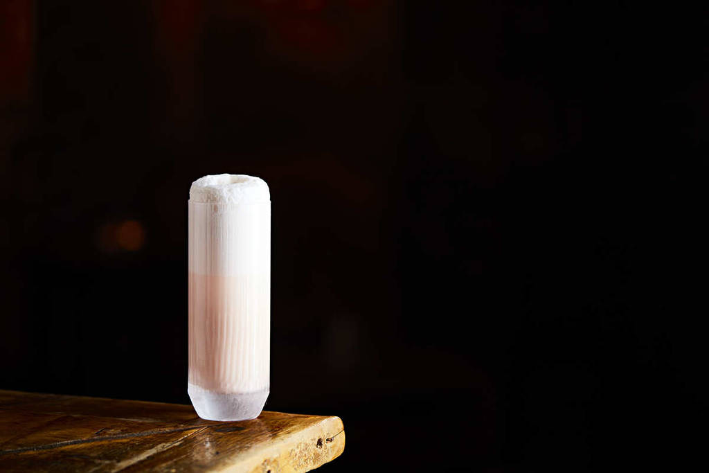 a pink cocktail in a tall glass perched on the wooden edge of a bar