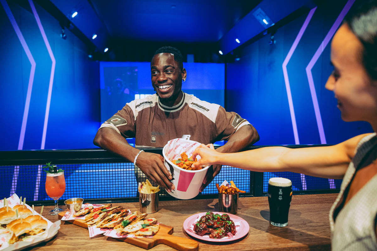 someone holding out a bucket of fried chicken over a table of food at toca social. Their friend is helping themselves to a piece of chicken from the bucket