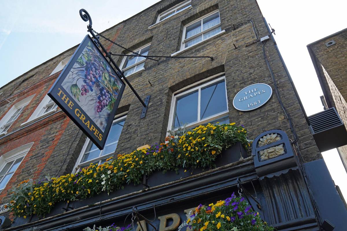 the exterior of the grapes pub, looking up above the entrance at the hanging sign showing a bunch of grapes