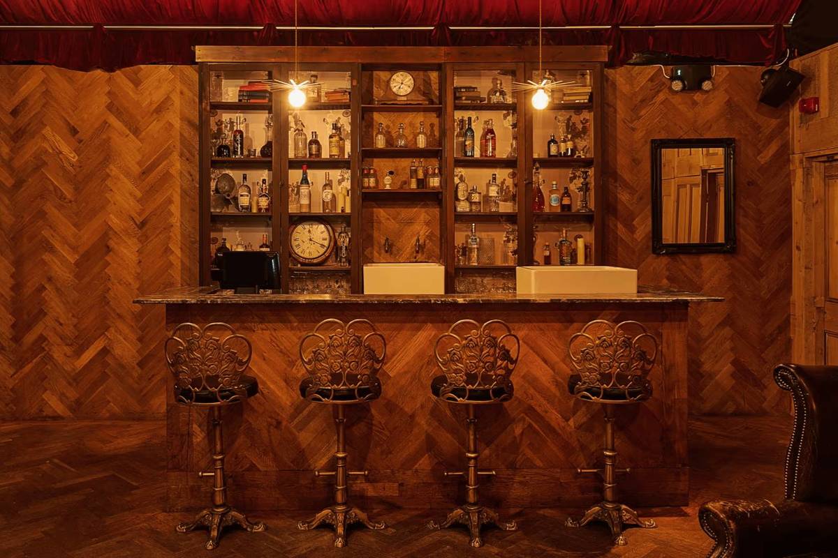 a wood panelled secret bar with a period cocktail and old-timey looking bar stools