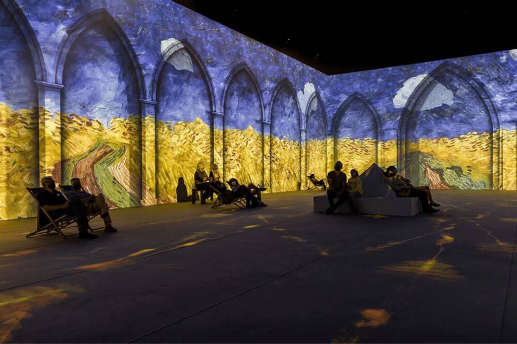 people sit and watch projections of Van Gogh's wheat field paintings at the immersive Van Gogh Exhibition