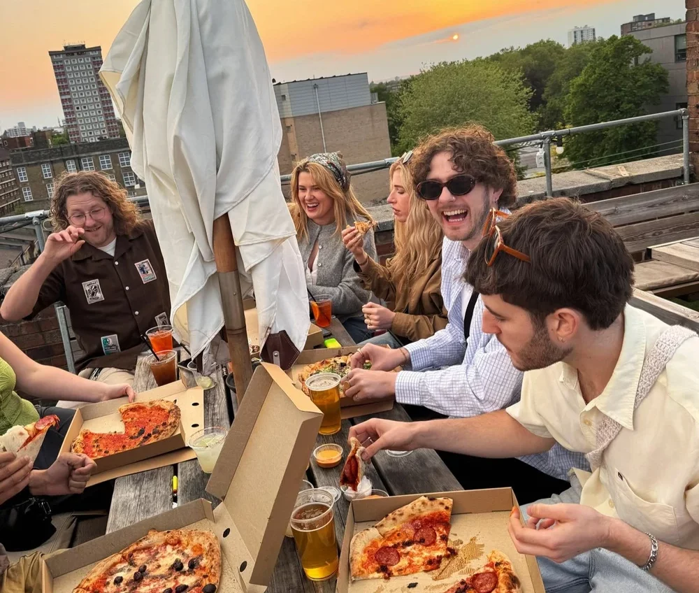 A group of friends enjoying pizza from the box on an east London rooftop