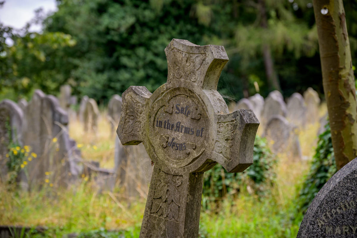 a cross shaped grave marker in a cemetery bearing the inscription 'safe in the arms of jesus'