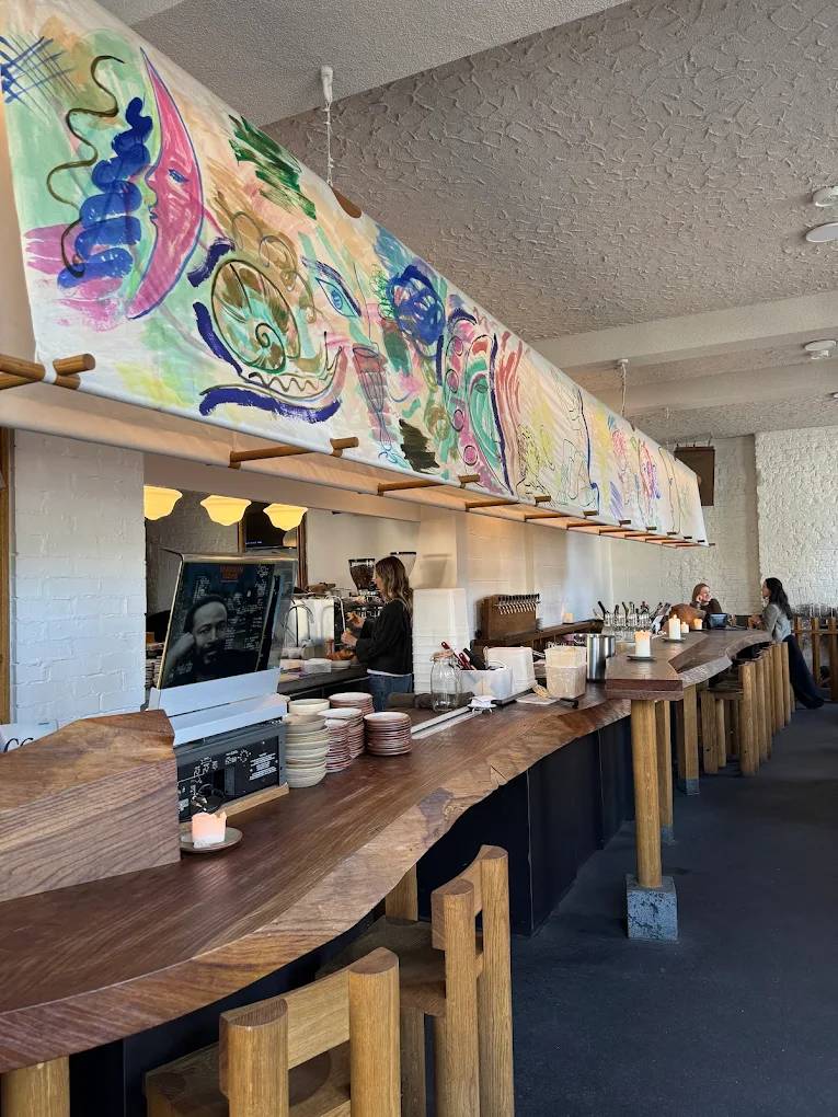 the interior of goodbye horses wine bar, with a long wooden curving bar beneath colourful paintings
