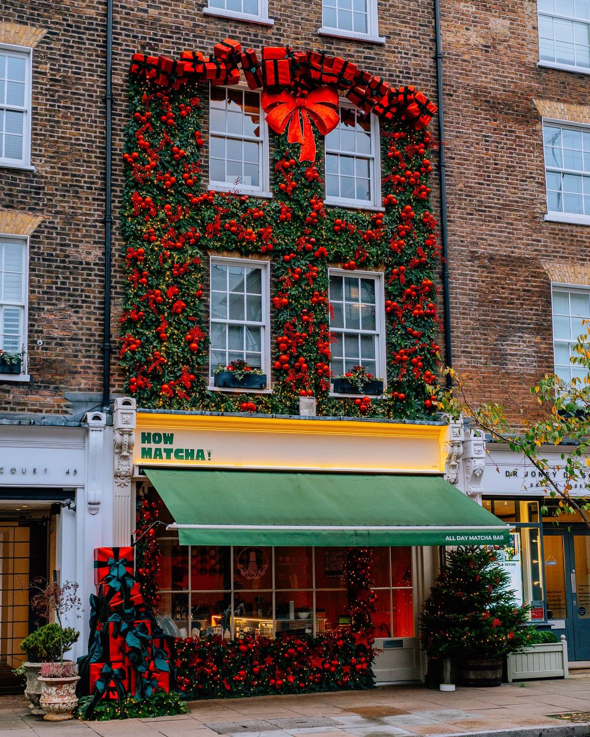the exterior of a 'how matcha' store, transformed into a red and green christmas present with an ornate floral display taking over the facade