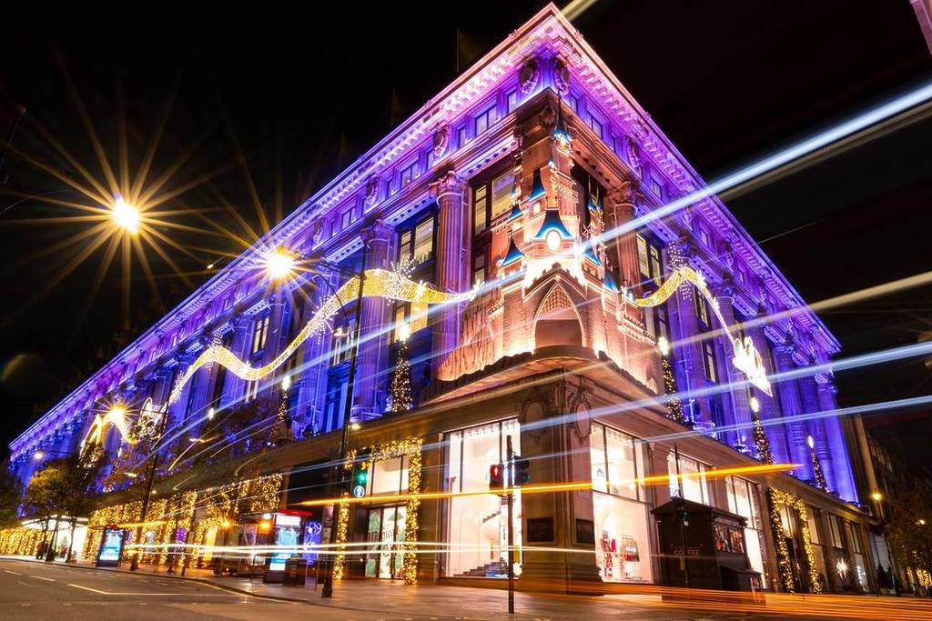 the selfridges store in london decrated with swooping golden fairy lights and a repesentation of the iconic disneyland castle on the corner of the building