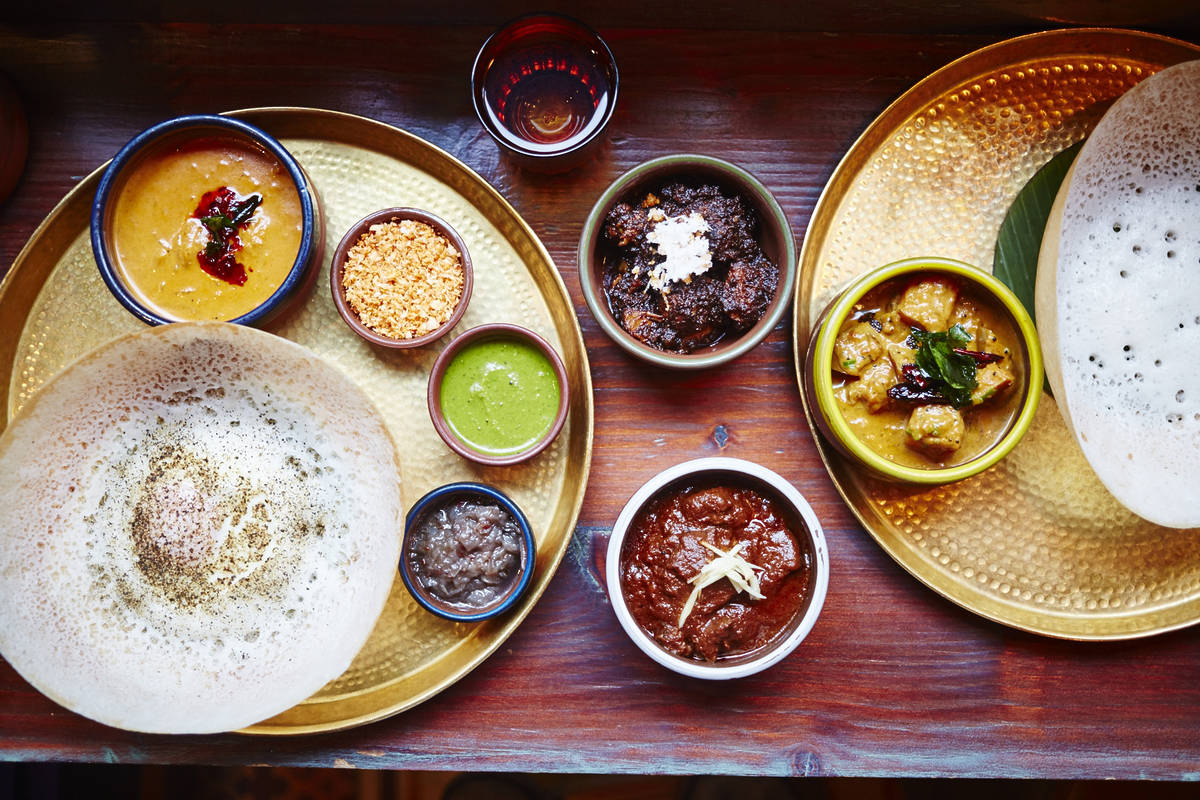 a table laid with large 'hoppers' alongside chutneys, stews, curries, and more