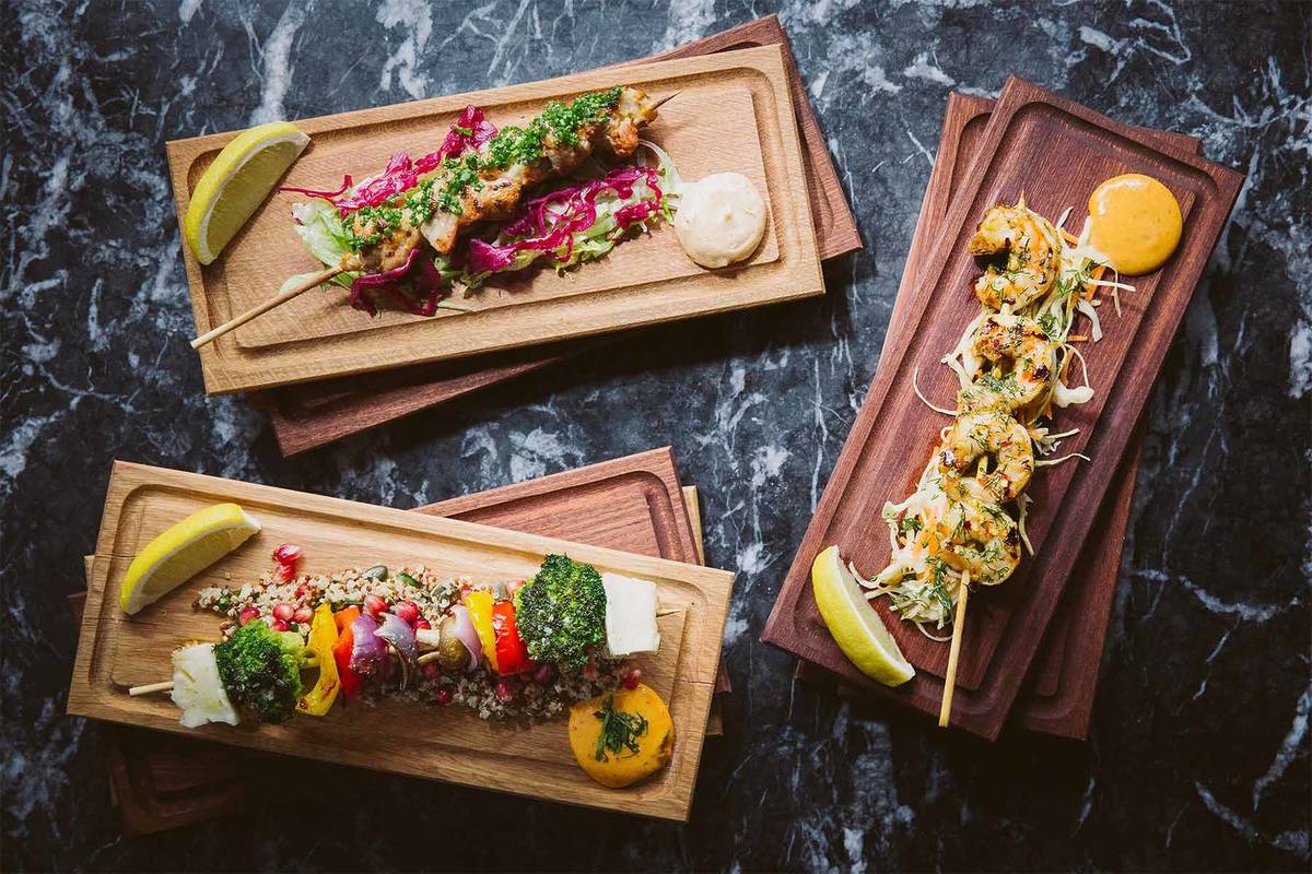 three different skewers of suvlaki each presented on an individual wooden chopping board