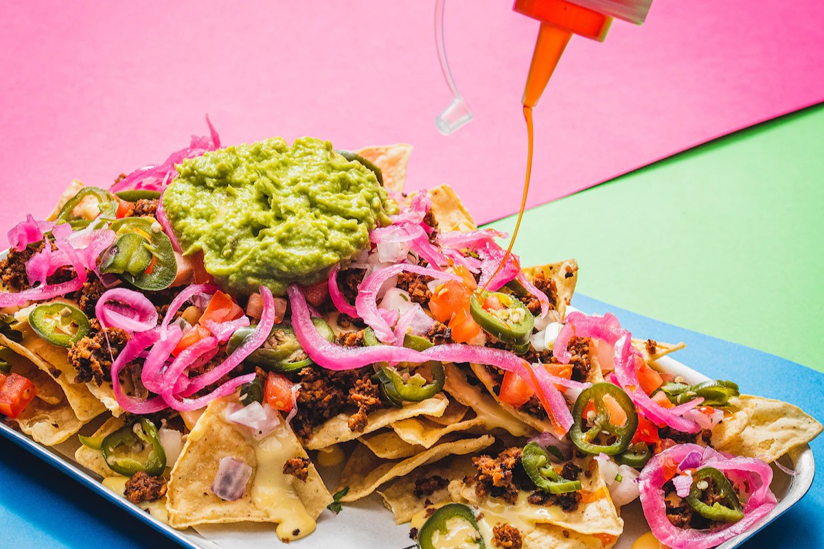 a plate of nachos covered with toppings, being drizzled with a spicy oil