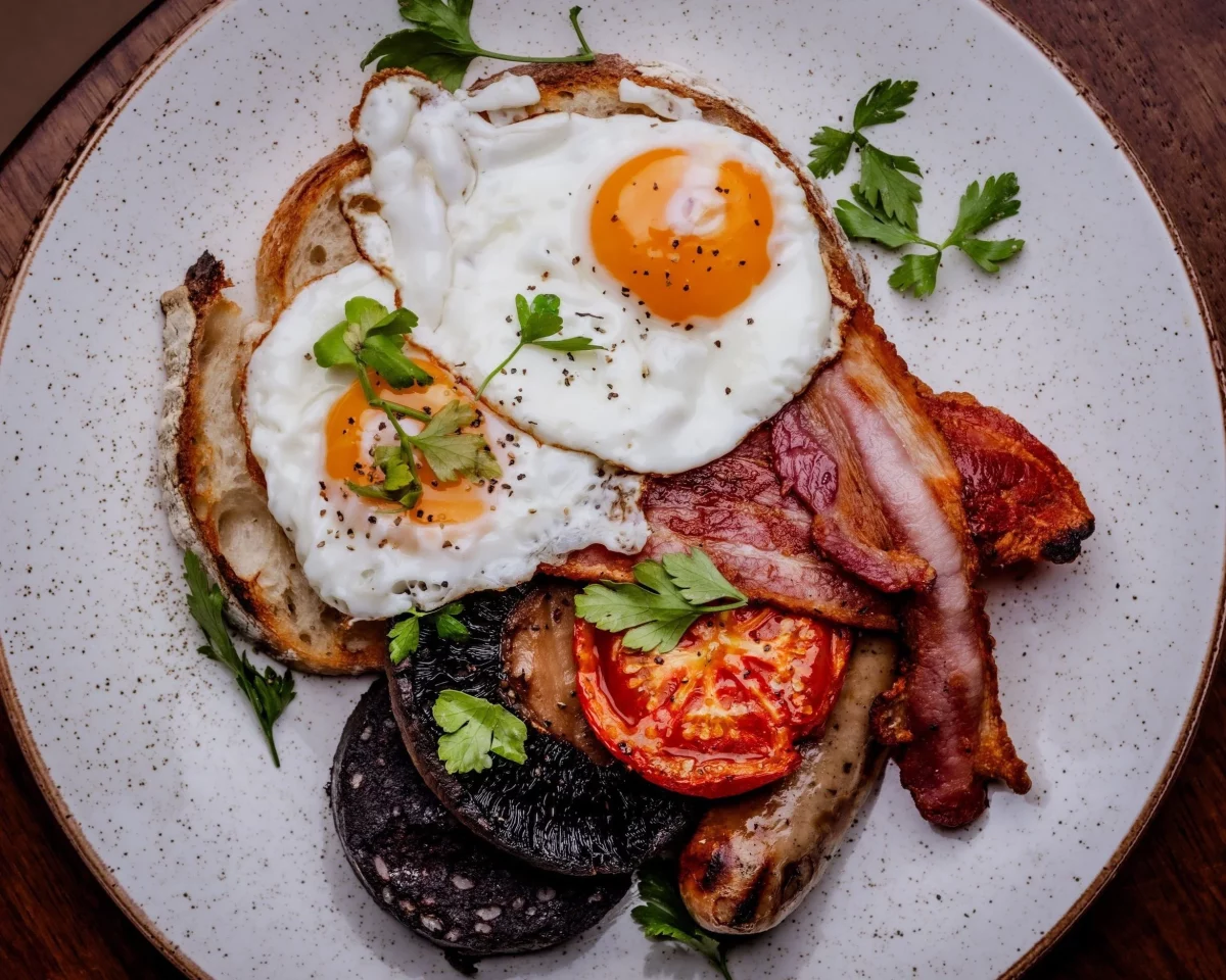 a fancy looking version of a full english, with fried eggs, bacon, tomato, black pudding, piled on a plate