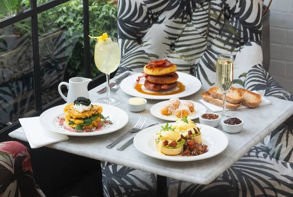 a table laid out for brunch with glassses of cocktail and prosecco as well as plates of pancakes, eggs benedict, and more