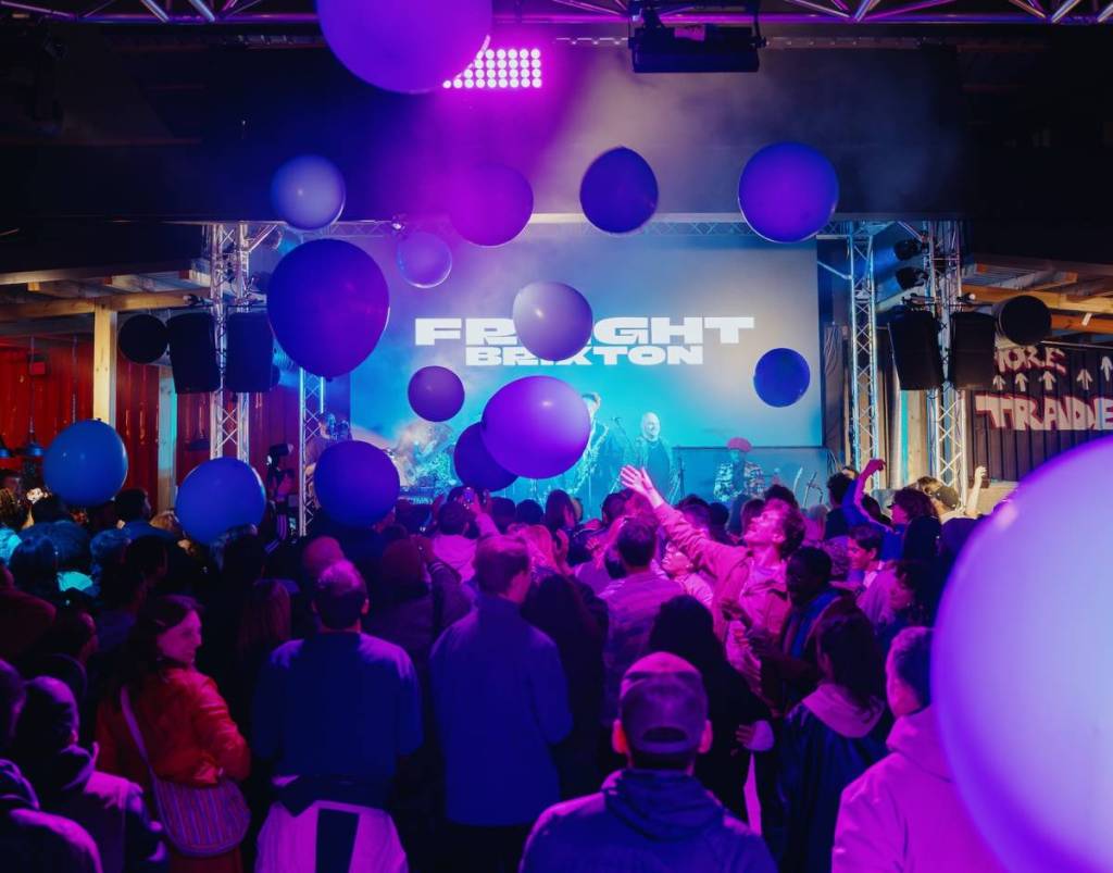 la gente balla in un locale illuminato di viola con palloncini che cadono dal soffitto