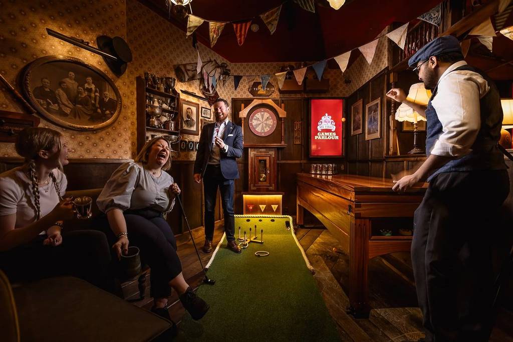 un groupe de personnes rit dans une cabine de style victorien au Mr Foggs City Tavern, rempli de jeux tels que les fléchettes, le beer pong et le mini-golf