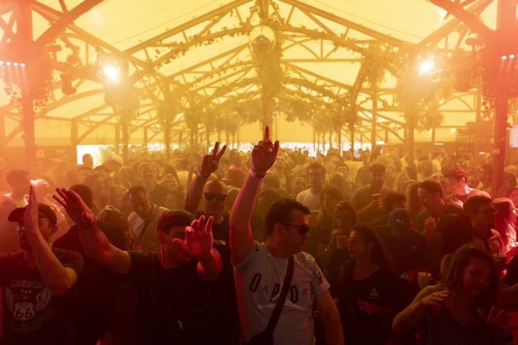 a crowd dances in a giant tent with a hazy, golden-tinted lighting
