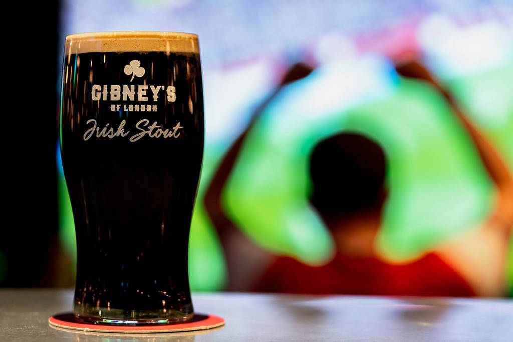 a pint of Gibney's stout in the foreground, in front of someone celebrating while watching sport